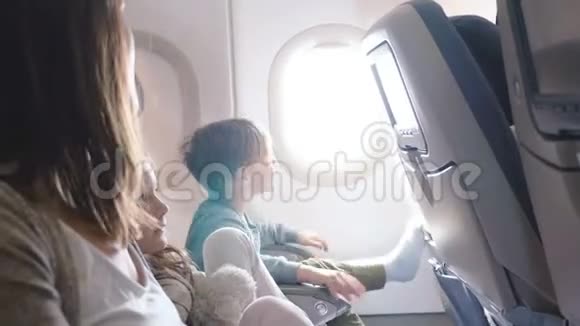 快乐的小男孩在飞行中关闭飞机窗盖看着相机微笑着与家人一起旅行视频的预览图
