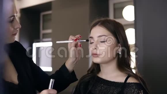 专业Visagist深色头发的女性使用化妆刷进行完美的红色美甲在眼睑上涂抹眼影视频的预览图