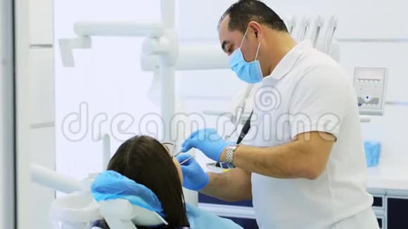 牙医对坐在牙科椅上的年轻妇女进行预防性检查视频的预览图