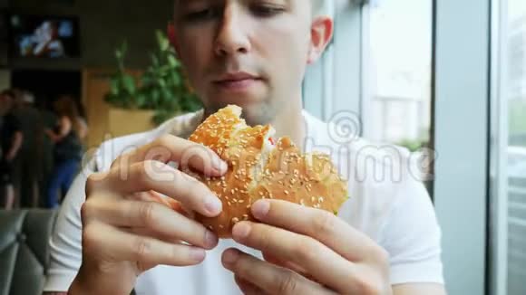 一位饥饿的年轻人在咖啡馆快餐店吃汉堡视频的预览图