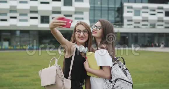 两个美丽的无忧无虑的女孩用智能手机自拍女人做滑稽的脸最好的朋友拍照视频的预览图