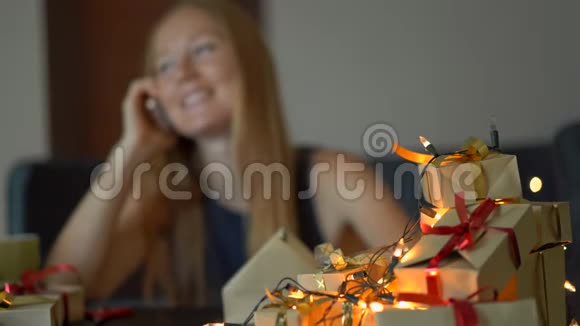 一个年轻的女人收拾礼物用手机说话现在用工艺纸包裹着红色和金色的丝带视频的预览图