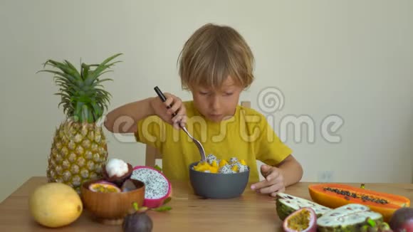 一个穿着黄色衬衫的小男孩在桌上吃芒果龙果和许多热带水果视频的预览图