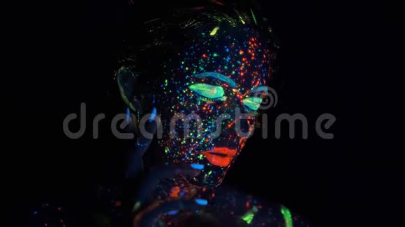 在女孩的脸上涂上了发光颜料一个美丽的年轻女子的肖像她的脸上有发光的油漆视频的预览图