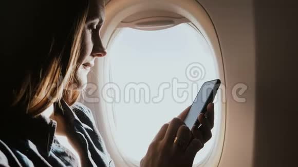 在飞机飞行期间在靠窗的座位上使用智能手机移动办公应用程序特写漂亮的年轻专注女商人视频的预览图