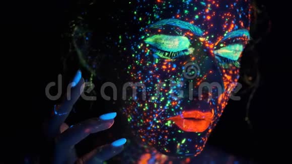女孩的脸上溅着发光的油漆霓虹灯下一个年轻女人的肖像视频的预览图
