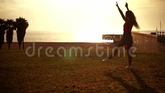 快乐的女孩跳起来在海滩上做翻车享受日落视频的预览图