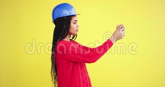 严肃的年轻女工程师在一个有黄色背景墙的工作室里用她的想象手机拍照视频的预览图