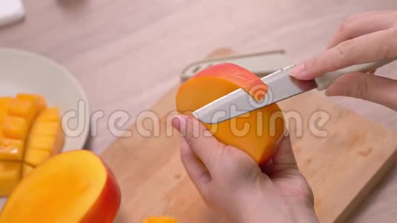 年轻女子正在切一个漂亮的新鲜多汁的芒果放在木桌上吃厨房里的砧板上4K视频的预览图