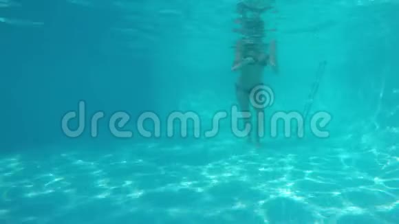 穿着比基尼的白人女孩在蓝色游泳池的镜头前在水下跳舞从水下观看视频的预览图