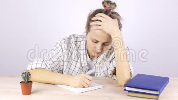 一个疲惫的学生订婚了坐在一张有课本的桌子旁睡着了视频的预览图