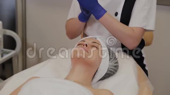 专业美容师用擦洗油涂在女人的脸上用她的手按摩视频的预览图