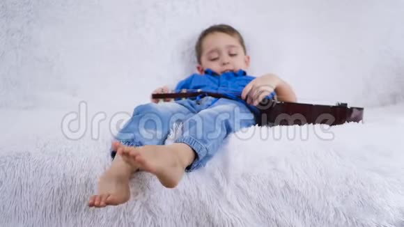 小男孩弹吉他躺在沙发上孩子晃着一腿唱歌集中注意力视频的预览图