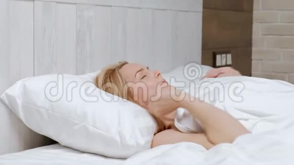 年轻迷人的中年金发女人穿着白色外套早上在床上醒来视频的预览图