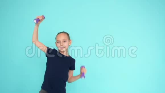 在绿松石背景下的健美操健身操中一个快乐的少女举起哑铃视频的预览图
