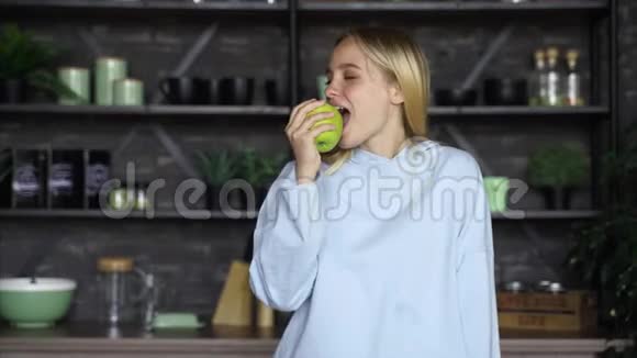 快乐的年轻女人在厨房里吃绿色苹果视频的预览图