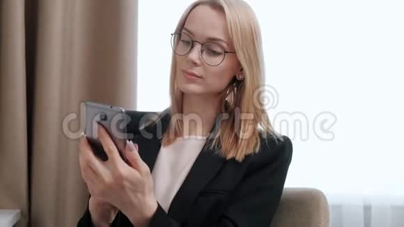 年轻迷人的中年金发女人穿着黑色商务套装戴着眼镜在酒店房间里在视频的预览图