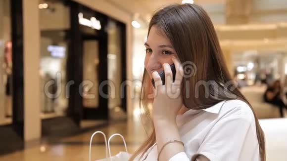 女孩坐在长凳上用商场里的电话视频的预览图