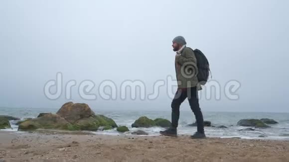 一个带背包的有胡子的时髦旅行者沿着海滩散步视频的预览图
