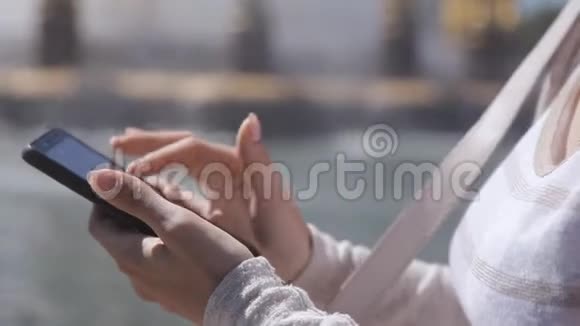 在炎热的夏天穿着米色西装坐在公园喷泉旁的智能手机的快乐女孩视频的预览图