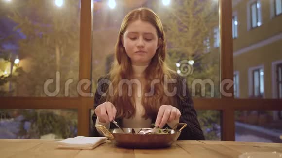 在现代咖啡馆里一位红头发的年轻女子享受着她的美食女孩用叉子和刀子吃沙拉视频的预览图