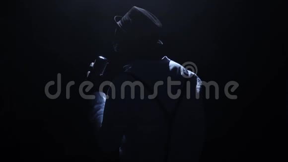 歌手在黑暗中微弱的灯光在麦克风唱着这首歌黑色背景剪影慢动作视频的预览图