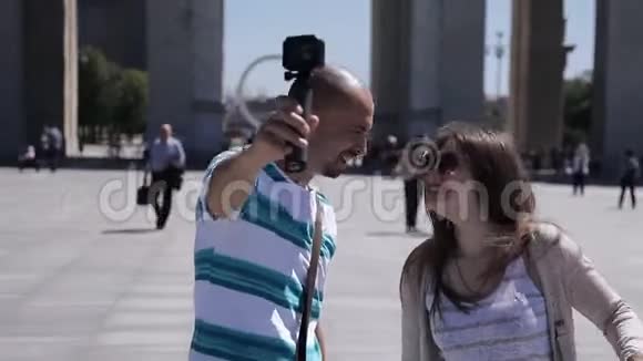 一对年轻的夫妇一男一女正沿着城镇广场散步并在镜头下拍摄自己游客游览视频的预览图
