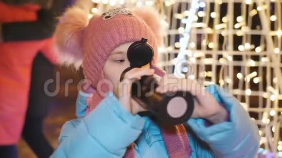 那个小女孩在城里的圣诞晚会上喝着热水瓶里的热茶视频的预览图