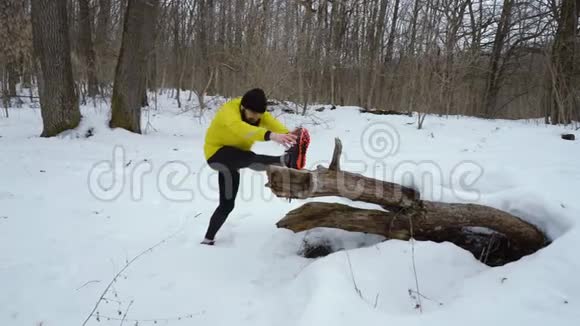 穿着黄色外套的蓄须运动员在冬天的森林里雪天伸腿视频的预览图