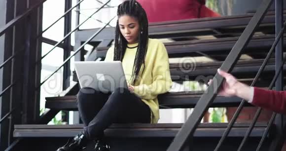 在现代建筑的办公室里一位非洲女士坐在楼梯上在办公室旁边的笔记本上打字视频的预览图