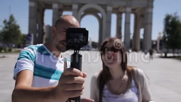 一对年轻的夫妇一男一女正沿着城镇广场散步并在镜头下拍摄自己游客游览视频的预览图