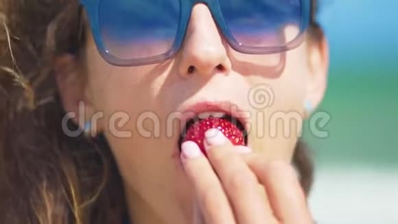 阳光明媚的夏天女人在海边吃草莓特写镜头视频的预览图