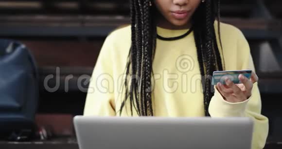 肖像非洲漂亮的女士用她坐在楼梯上的信用卡从她的笔记本网上订购了一些东西视频的预览图