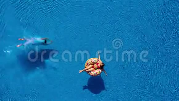 当女孩躺在甜甜圈泳池的浮球上时男人的空中景色潜入泳池视频的预览图