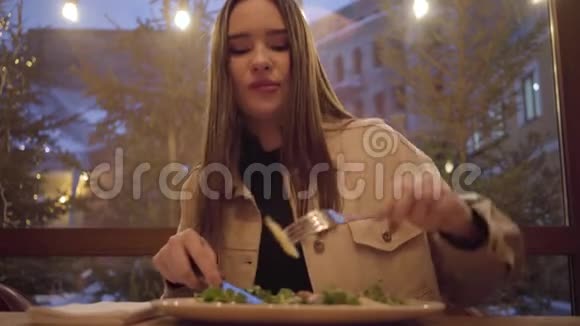 漂亮的年轻女孩吃沙拉用叉子和刀关闭孤独的女士在家里的餐馆或咖啡馆里度过时光视频的预览图