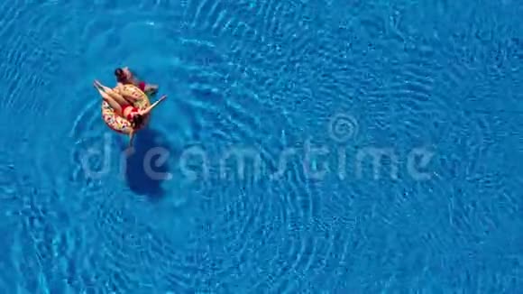 鸟瞰情侣在游泳池里玩男人在游泳女人躺在充气甜甜圈上视频的预览图