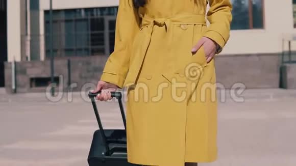 穿着黄色雨衣留着深色长发的时髦女人带着行李摘下眼镜环顾四周微笑着视频的预览图