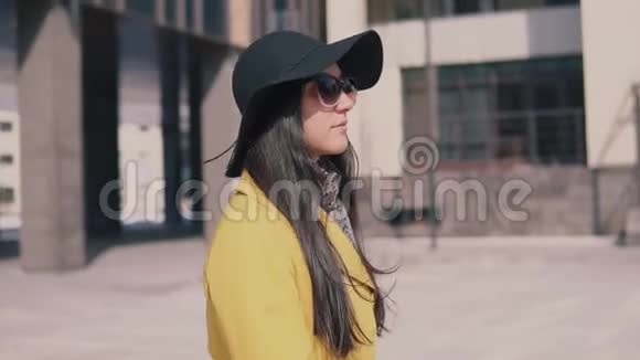 穿着黄色外套戴着深色长发戴着帽子的时髦女孩走在街上摘下眼镜看着前方视频的预览图