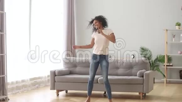 非洲女人在家里拿着智能手机跳舞听音乐视频的预览图