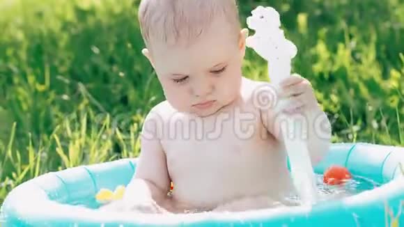 夏天小可爱的小男孩在草坪上的充气游泳池里玩着泼水视频的预览图