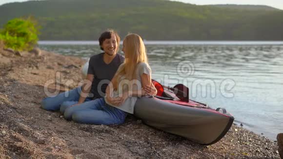 年轻的男人和女人坐在湖边或海滨的充气皮艇旁慢镜头视频的预览图