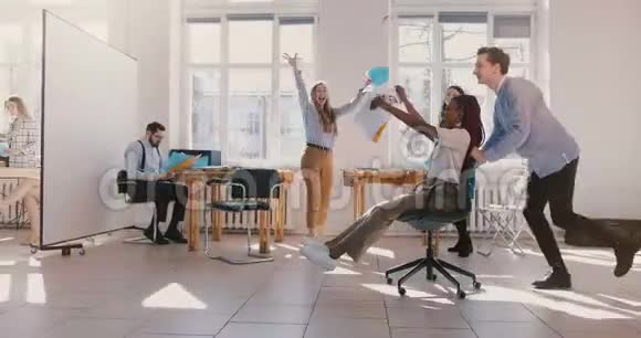 慢动作疯狂有趣的非裔美国女商人坐在椅子上玩得开心在健康的现代办公室庆祝视频的预览图