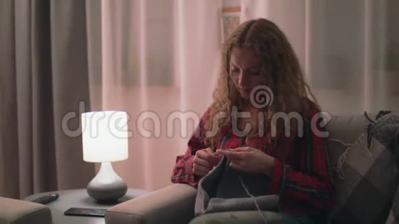 在舒适的家中坐在沙发上编织的中弹女子视频的预览图