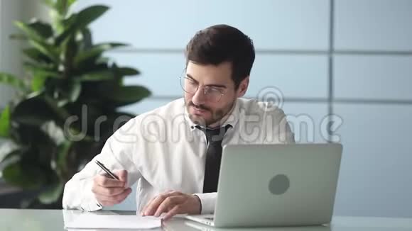 专注于工作的商人在工作场所看笔记本电脑做笔记视频的预览图