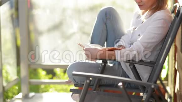 年轻美丽的女孩的肖像与白种人的外观阅读有趣的书坐在阳台上女人在放松视频的预览图