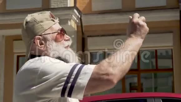戴太阳镜戴帽子的老人在城里散步并拍照留念视频的预览图