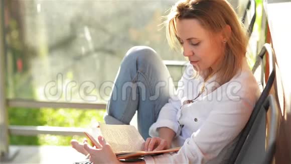 年轻美丽的女人在露台上阅读有趣的书在阳光明媚的日子里视频的预览图