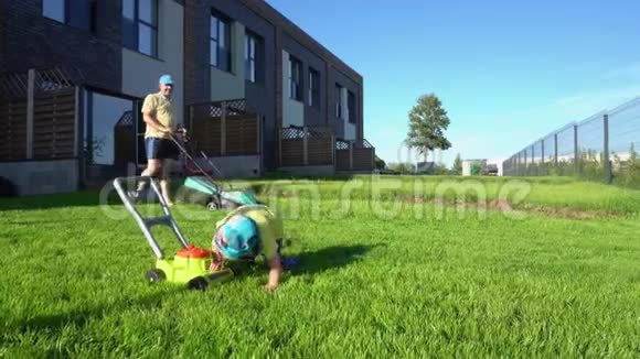 男人用割草机割草而儿子则玩玩具割草机万向节视频的预览图