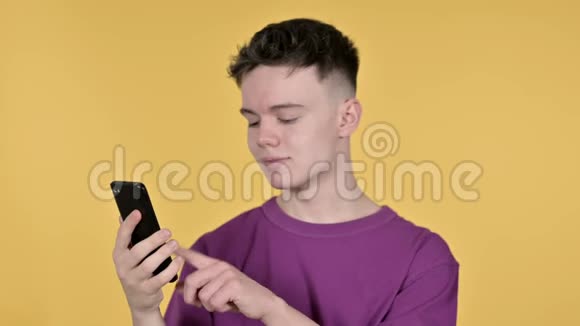 黄色背景下的年轻人浏览智能手机视频的预览图