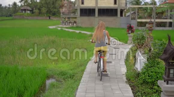 一个年轻的女人骑着自行车穿过美丽的稻田前往东南亚的概念慢镜头视频的预览图